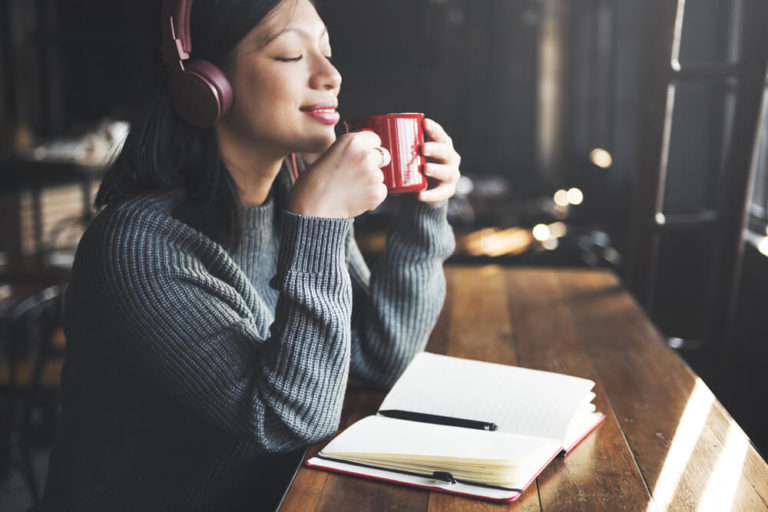 Woman drinking coffee with eyes closed and wearing headphones